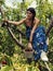 Beautiful young woman climbed on a cherry tree picking fruits and holding wooden bucket full of red ripe cherries