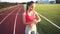 Beautiful young woman configures a program on her bracelet and running on athletic track on stadium at sunrise