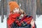 Beautiful young woman is cuddling little dog wrapped in red checkered plaid on a walk in winter forest