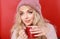 Beautiful young woman with cup of hot drink on red background.