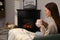 Beautiful young woman with cup of hot drink sitting on sofa near fireplace. Space for text