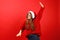 A beautiful young woman dances carelessly and enjoys Christmas music in headphones on a red background. Holiday dance playlist