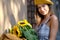 Beautiful young woman with dark hair in a hat, in the city, holding hands for a bouquet of sunflowers and looking away.