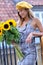 Beautiful young woman with dark hair in a hat, in the city, holding hands for a bouquet of sunflowers and looking away.