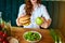 Beautiful young woman decides eating hamburger or apple in kitchen. Cheap junk food vs healthy diet