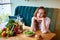 Beautiful young woman decides eating hamburger or vegetables  in kitchen. Cheap junk food vs healthy diet