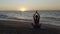 Beautiful young woman doing sitting yoga on the beach while watching the sunset.