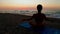 Beautiful young woman doing sitting yoga on the beach while watching the sunset.