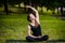 Beautiful young woman doing stretching exercise on green grass at park. Yoga workout