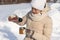 A beautiful young woman in a down jacket and mittens pours a hot drink into a mug from a thermos in nature on a sunny winter day.