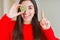 Beautiful young woman eating half fresh green kiwi surprised with an idea or question pointing finger with happy face, number one