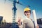 A beautiful young woman engineer is in front of a construction crane wearing protective gear, helmet and glasses,taking a selfie p