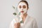 Beautiful young woman with facial mask and eucalyptus branch on light background