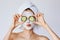 Beautiful young woman with facial mask on her face holding slices of cucumber. Skin care and treatment, spa, natural beauty and