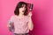 Beautiful young woman feels frightened while holding hairspray and looks at hairbrush which entangled in hair. Charming girl wears