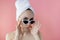 Beautiful young woman in glasses with a towel on her head after bath on pink background