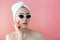 Beautiful young woman in glasses with a towel on her head after bath on pink background