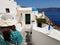 Beautiful young woman in green dotted dress walking in Oia, Santorini streets. White houses, blue sea