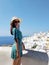 Beautiful young woman in green dotted dress walking in Oia, Santorini streets. White houses, blue sea