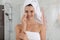 Beautiful young woman with hair wrapped in towel cleaning her face indoors