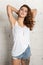 Beautiful young woman with hands behind head. White brick wall, not isolated