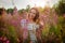 Beautiful young woman with a happy smile clinging to the high stems herb Kipray with pink flowers