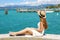 Beautiful young woman with hat sitting on wall looking at stunning landscape of Garda Lake in Sirmione, Italy