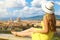Beautiful young woman with hat sitting on wall looking at stunning panoramic view of Florence in Tuscany, Italy