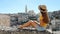 Beautiful young woman with hat sitting on wall looking at stunning panoramic view of Matera City in Italy. Slow motion.