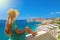 Beautiful young woman with hat sitting on wall looking at stunning panoramic village of Dubrovnik in Croatia, Europe