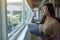 A beautiful young woman with headphone looking outside the window while working on laptop computer