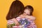 Beautiful young woman and her charming little daughter hugging indoor. Child congratulates mom with Mother`s Day, gives flowers,