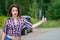 Beautiful young woman hitchhiking gesture at countryside, broken car on background