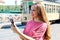 Beautiful young woman holding smart phone in her hands in street with old tram passing on the background in Milan, Italy