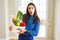 Beautiful young woman holding wooden box full of healthy groceries scared in shock with a surprise face, afraid and excited with