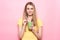 Beautiful young woman holds green smoothie with straw and smiling near pink wall.