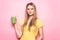 Beautiful young woman holds green smoothie with straw and smiling near pink wall.
