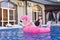 Beautiful young woman with inflatable flamingo in blue swimming pool