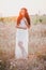 Beautiful young woman with long curly hair dressed in boho style dress posing in a field with dandelions