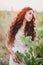 Beautiful young woman with long curly hair dressed in boho style dress posing in a field with dandelions