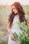 Beautiful young woman with long curly hair dressed in boho style dress posing in a field with dandelions