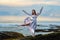 Beautiful young woman in long dress waving in the wind stay on ocean beach on the rock on sunset in Bali Indonesia