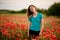Beautiful young woman with long hair standing on field with red poppies.