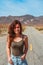 Beautiful young woman with long hair walks along a picturesque empty road in Death Valley overlooking the mountains, USA