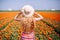 Beautiful young woman with long red hair wearing a striped dress and straw hat standing by the back on colorful tulip field