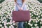 Beautiful young woman with long red hair wearing in white dress standing with luggage on colorful tulip field