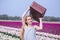 Beautiful young woman with long red hair wearing in white dress standing with luggage on colorful tulip field