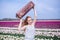 Beautiful young woman with long red hair wearing in white dress standing with luggage on colorful tulip field