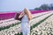 Beautiful young woman with long red hair wearing in white dress standing with luggage on colorful tulip field