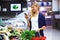 Beautiful young woman looking shopping list on mobile phone while buying fresh vegetables in the market.